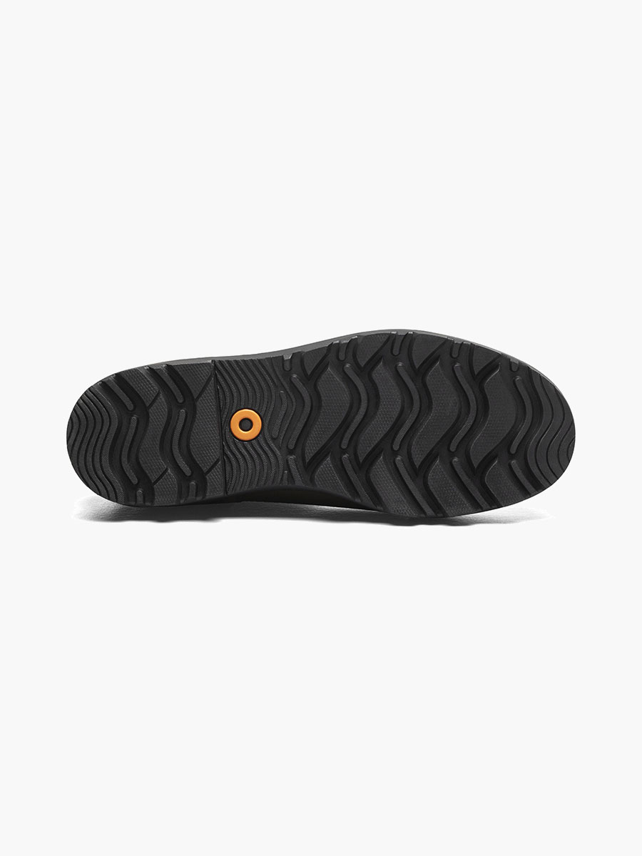 L'image montre la semelle d'une chaussure noire sur fond blanc. La semelle présente un motif ondulé et robuste, avec un détail orange circulaire près du centre.
