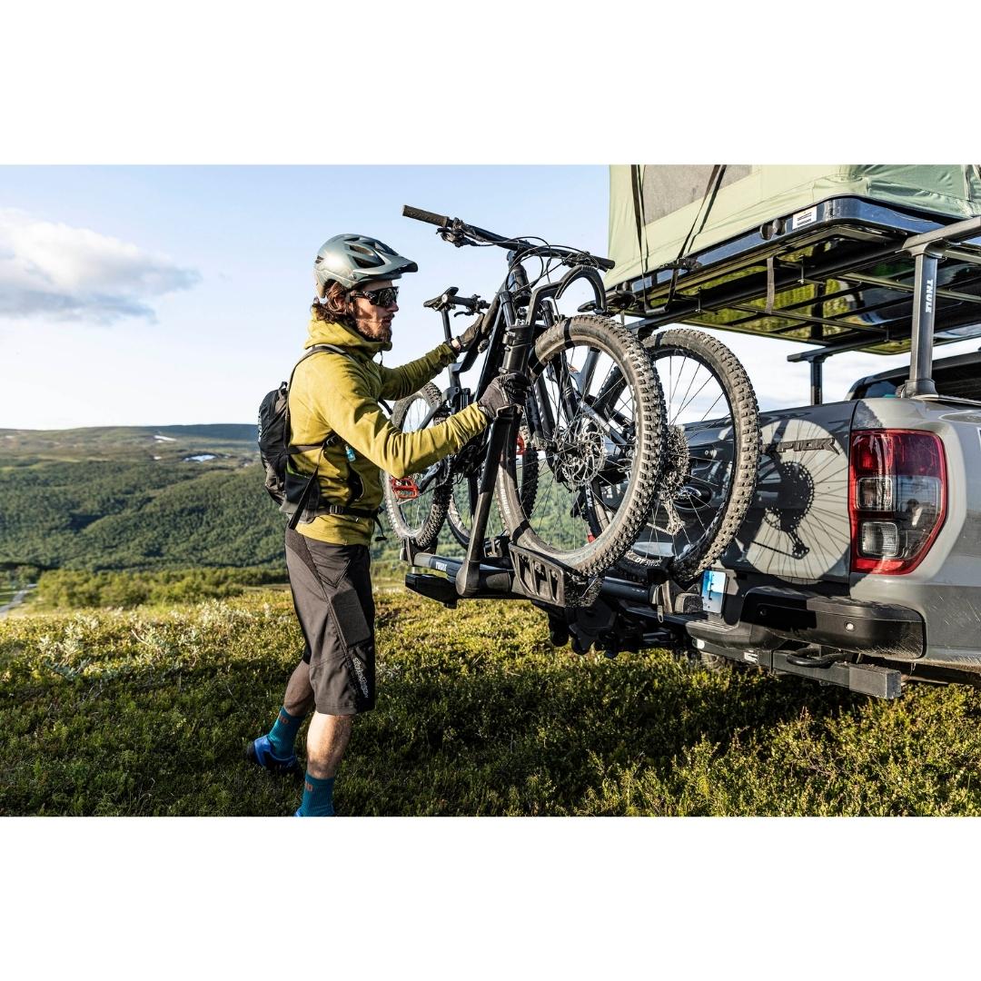 Thule T2 Pro XTR 2 - 1.25" installé sur une camionnette avec deux vélos sur le support et un homme qui manipule le vélo sur le support