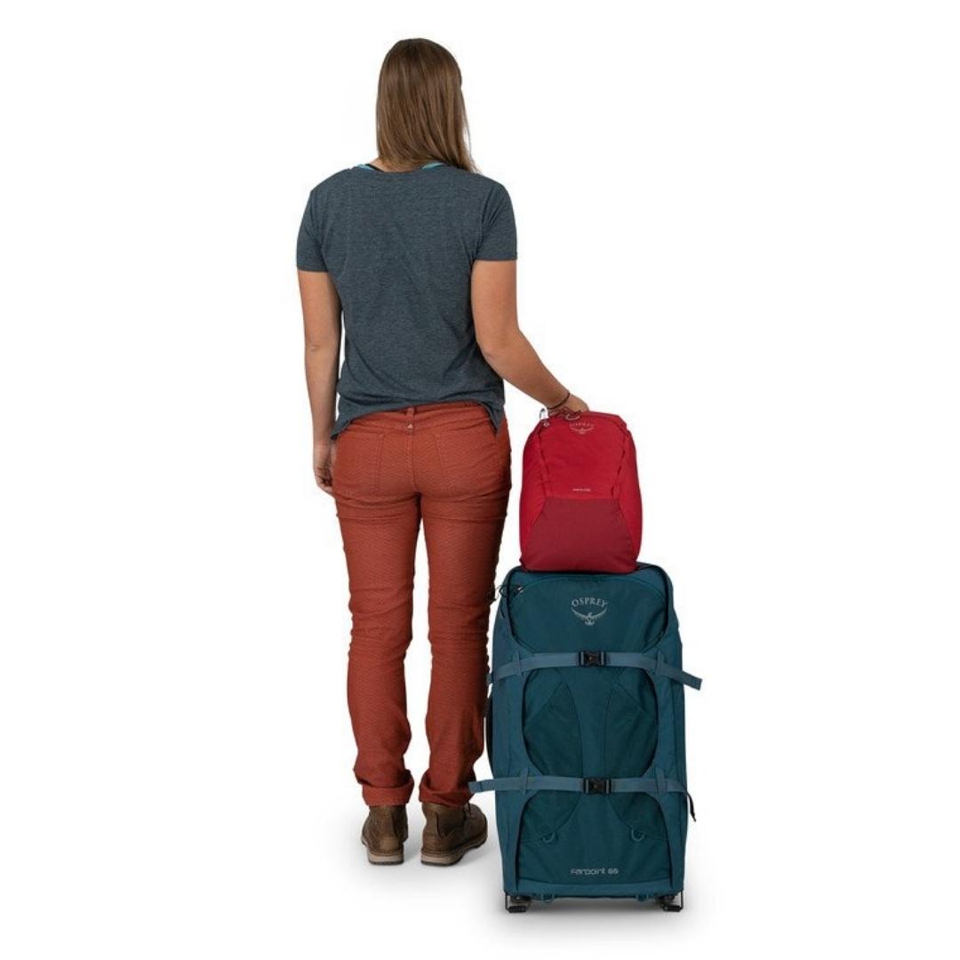 SAC À DOS OSPREY DAYLITE CINTRÉ ATTACHÉ A LA POIGNÉE DE TRANSPORT D'UNE VALISE ET UNE FEMME QUI TRANSPORTE L'ENSEMBLE