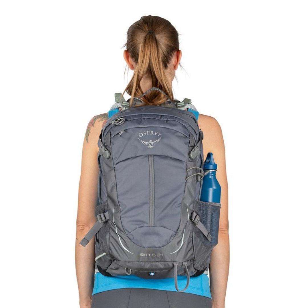 SAC À DOS OSPREY SIRRUS 24 POUR FEMME PORTÉ PAR UNE FEMME VUE DE DOS LE SAC AUX ÉPAULES AVEC UNE BOUTEILLE DANS LA POCHE LATÉRALE