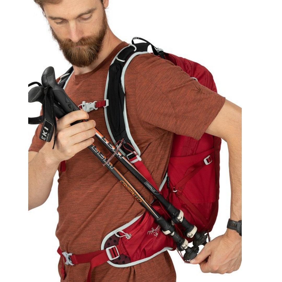 SAC À DOS OSPREY TALON 22 PORTÉ PAR UN HOMME QUI RANGE DES BÂTONS DE TREKKING