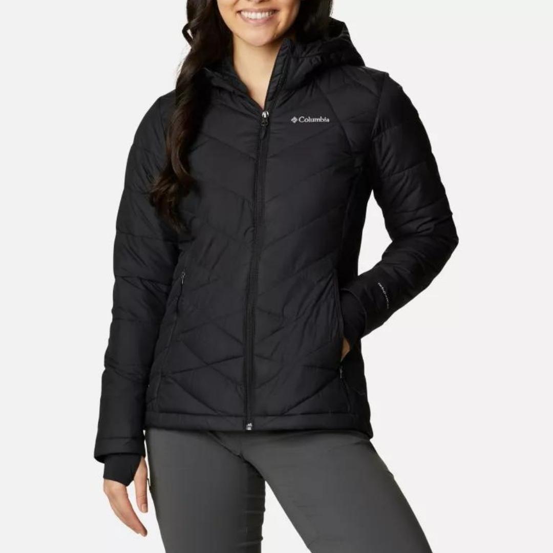 MANTEAU COLUMBIA HEAVENLY HOODED POUR FEMME COULEUR BLACK PORTÉ PAR UNE FEMME VUE DE FACE AVEC UNE MAIN DANS LA POCHE À MAIN À FERMETURE ÉCLAIR ET LE MANTEAU AVEC FERMETURE ÉCLAIR PLEINE LONGUEUR AU DEVANT