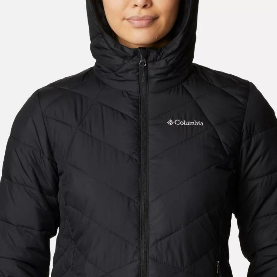 MANTEAU COLUMBIA HEAVENLY HOODED POUR FEMME COULEUR BLACK PORTÉ PAR UNE FEMME VUE EN GROS PLAN SUR LE HAUT DU MANTEAU LA FEMME PORTE LE CAPUCHON ET ON VOIT LE NOM DE LA MARQUE SUR LE DEVANT GAUCHE DU MANTEAU