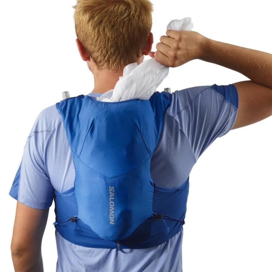 VESTE D'HYDRATATION SALOMON ADV SKIN 5 AVEC BOUTEILLES POUR HOMME couleur NAUTICAL BLUE / EBONY / WHITE porté par un homme qui retire un vêtement de la poche arrière principale