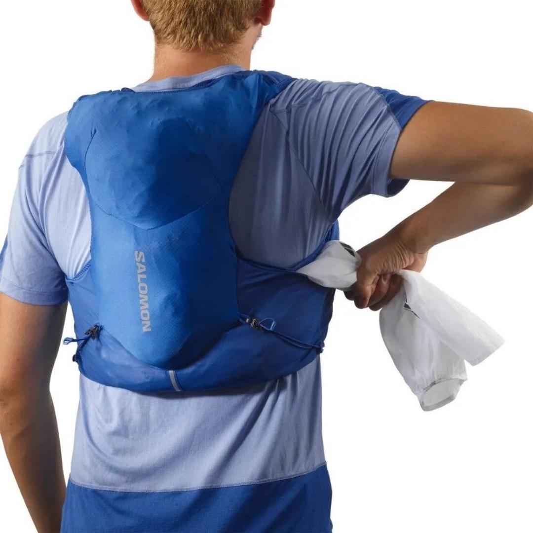 VESTE D'HYDRATATION SALOMON ADV SKIN 5 AVEC BOUTEILLES POUR HOMME couleur NAUTICAL BLUE / EBONY / WHITE portée par un homme qui retire une veste dans la poche latérale arrière