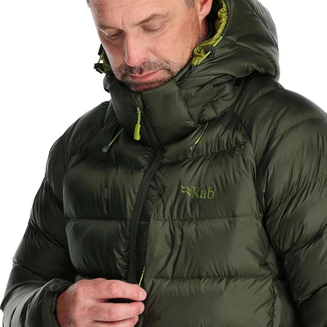 MANTEAU ISOLÉ EN DUVET RAB AXION PRO POUR homme couleur army porté par un homme qui ouvre la fermeture éclaire de la poche de poitrine à gauche du manteau vert on voit le nom RAB écrit en vert ton sur ton a gauche sur la poche de poitrine