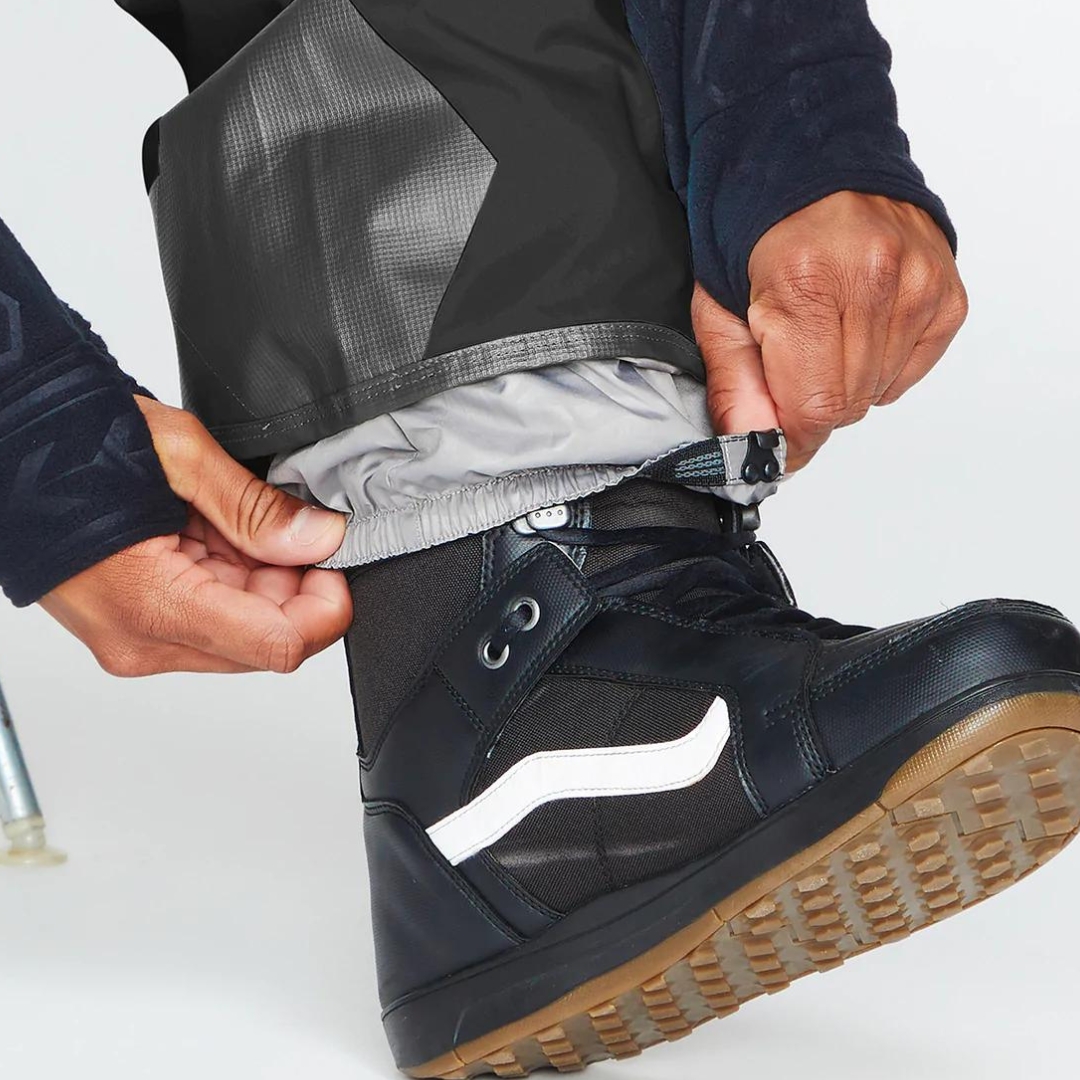 SALOPETTE ISOLÉE VOLCOM RAIN GORE-TEX POUR HOMME couleur black portée par un homme qui montre les guêtres interne à la cheville