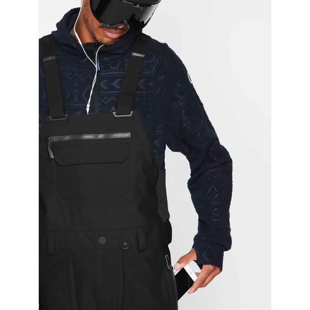 SALOPETTE ISOLÉE VOLCOM RAIN GORE-TEX POUR HOMME couleur black portée par un homme qui range son téléphone cellulaire dans la poche latérale