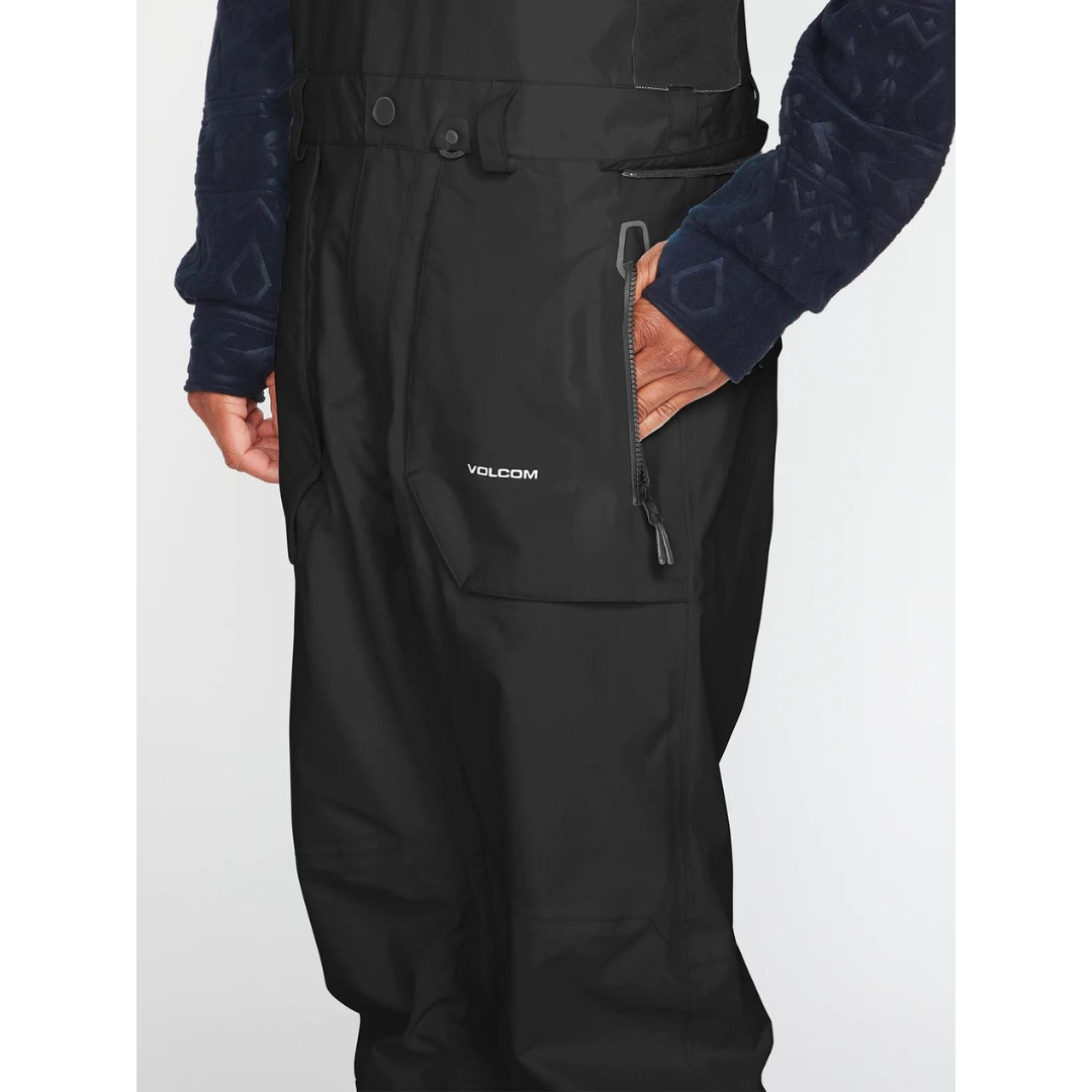 SALOPETTE ISOLÉE VOLCOM RAIN GORE-TEX POUR HOMME couleur black portée par un homme qui met la main dans sune poche latérale