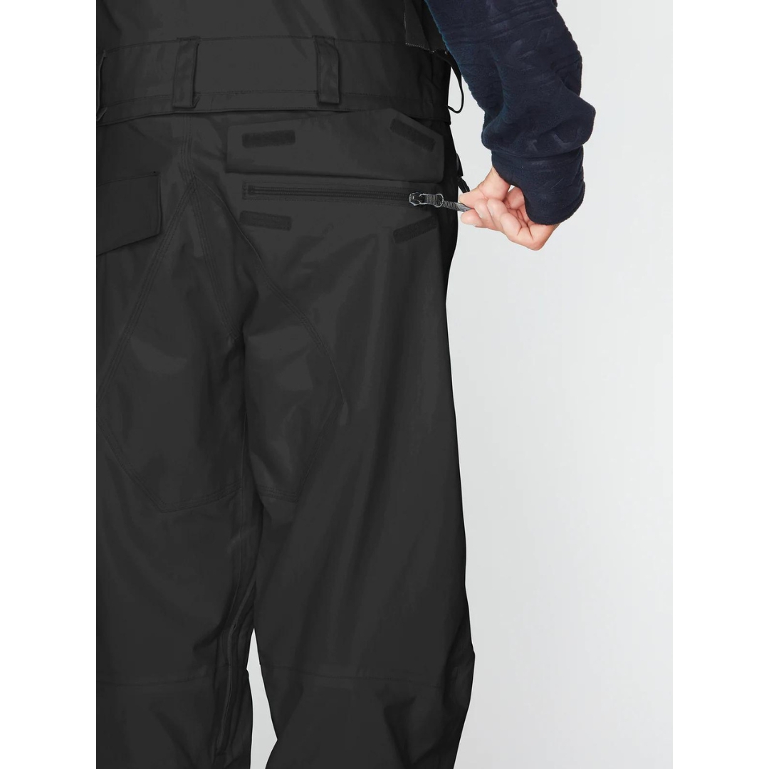 SALOPETTE ISOLÉE VOLCOM RAIN GORE-TEX POUR HOMME couleur black portée par un homme qui montre la poche arrière rabat ouvert, bandes velcro de fermeture visible ainsi que la fermeture à glissière de la poche
