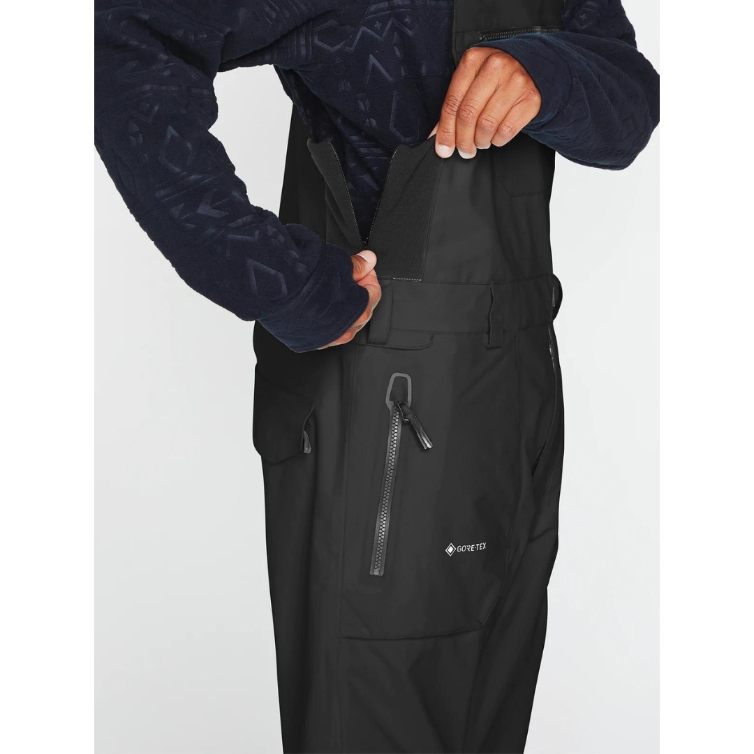 SALOPETTE ISOLÉE VOLCOM RAIN GORE-TEX POUR HOMME couleur black portée par un homme qui montre l'ouverture supplémentaire pour le haut de la salopette