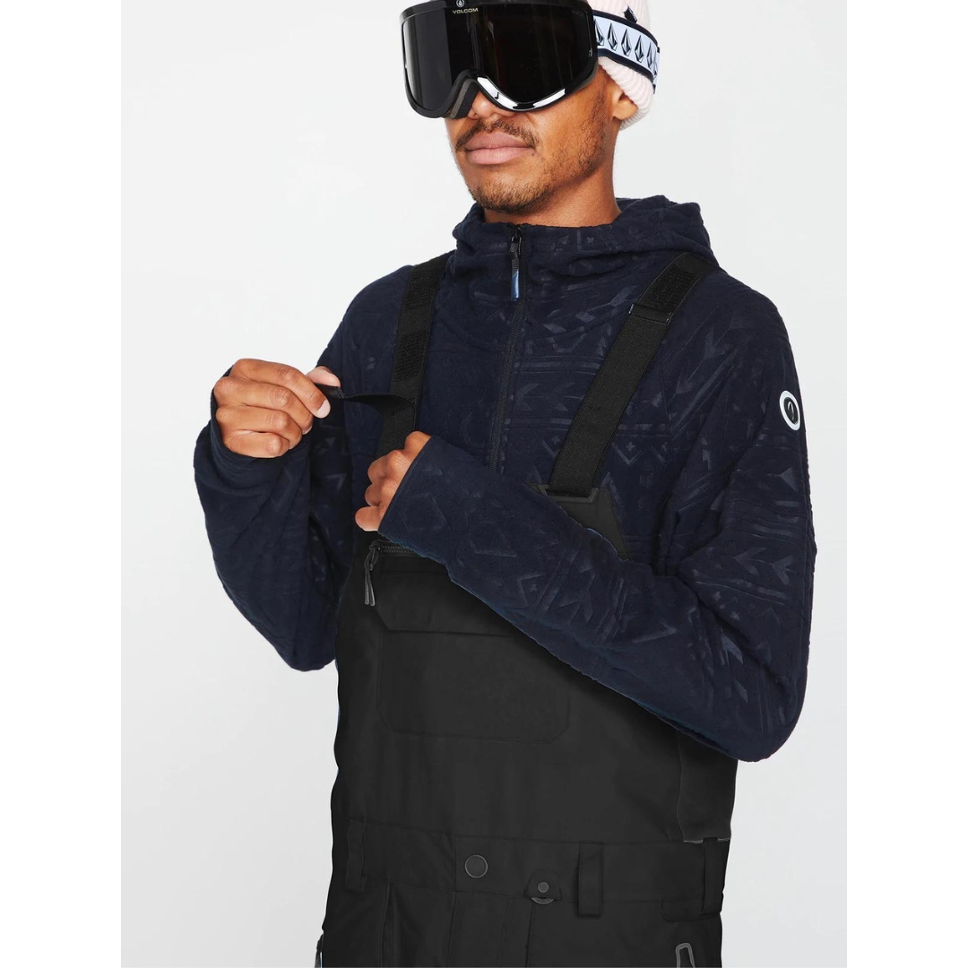 SALOPETTE ISOLÉE VOLCOM RAIN GORE-TEX POUR HOMME couleur black portée par un homme qui ajuste une bretelle avec la bande velcro facilement accessible