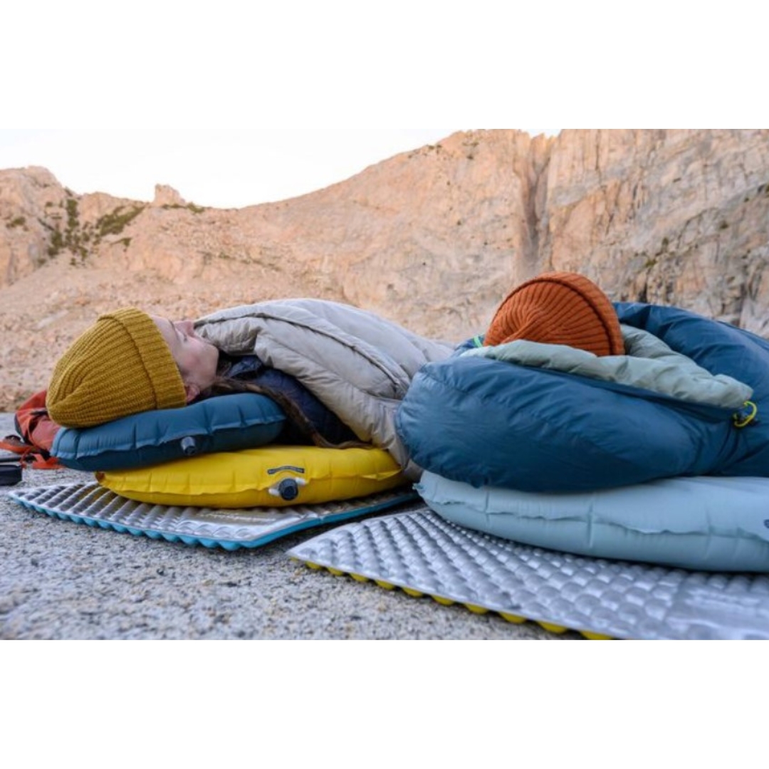 OREILLER DE CAMPING THERM-A-REST AIRHEAD LITE COULEUR DEEP PACIFIC DEUX PERSONNES COUCHÉES EN PLEIN AIR SUR DES MATELAS DE SOL ET SUR LE MATELAS NEOAIR AVEC L'OREILLER POUR LA PERSONNE DE GAUCHE