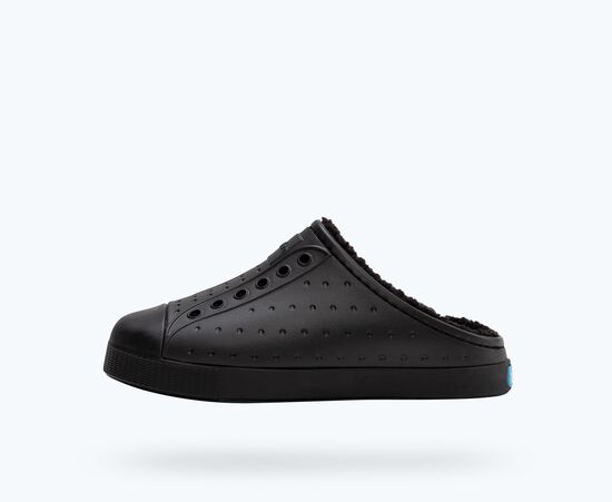 Une chaussure de sport noire à enfiler avec des détails perforés et une doublure douce, présentée sur un fond gris clair uni.