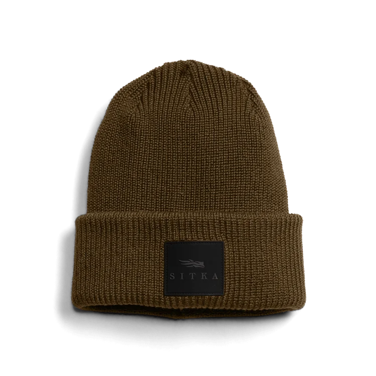 Bonnet en tricot marron avec un revers replié et un écusson rectangulaire noir avec le mot "SITKA" et un petit logo sur le devant.