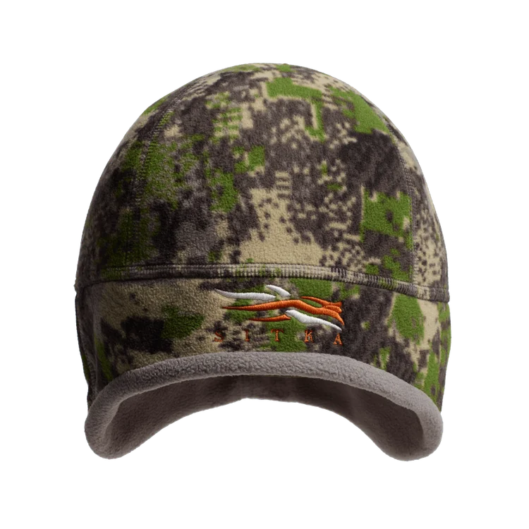 Un bonnet de chasse en polaire avec un motif de camouflage numérique vert, marron et beige et un logo Sitka orange brodé sur le devant. Le bonnet a une doublure intérieure grise et douce.