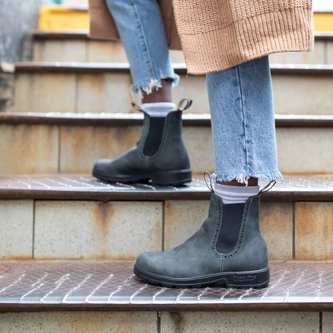 BOTTE URBAINE BLUNDSTONE 1630 MONTANTE ORIGINALE NOIR RUSTIQUE POUR FEMME VUE DES BOTTES DE COULEUR GRISE ET NOIRE PORTÉES PAR UNE FEMME DANS DES ESCALIERS