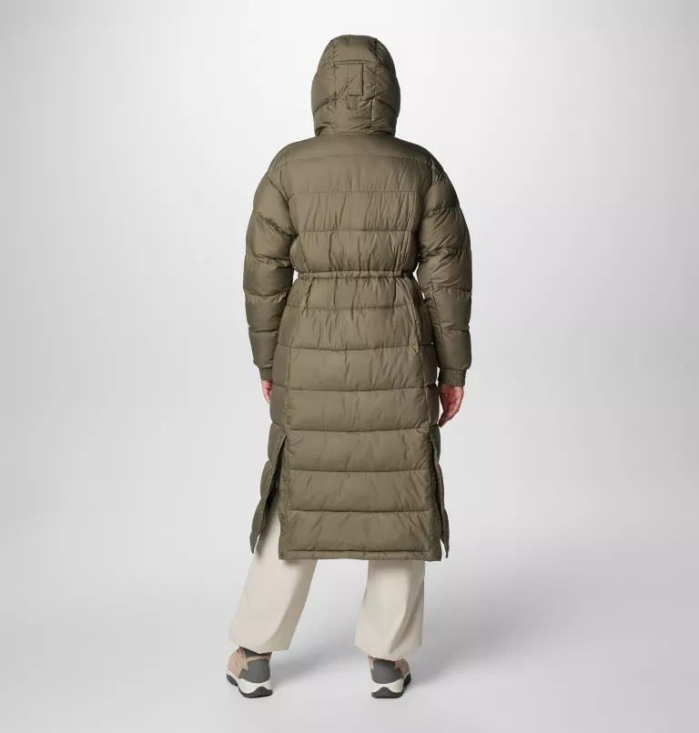 Une personne porte un long manteau matelassé vert olive avec une capuche et se tient dos à la caméra. Elle porte également un pantalon clair et des baskets grises. L'arrière-plan est gris clair uni.