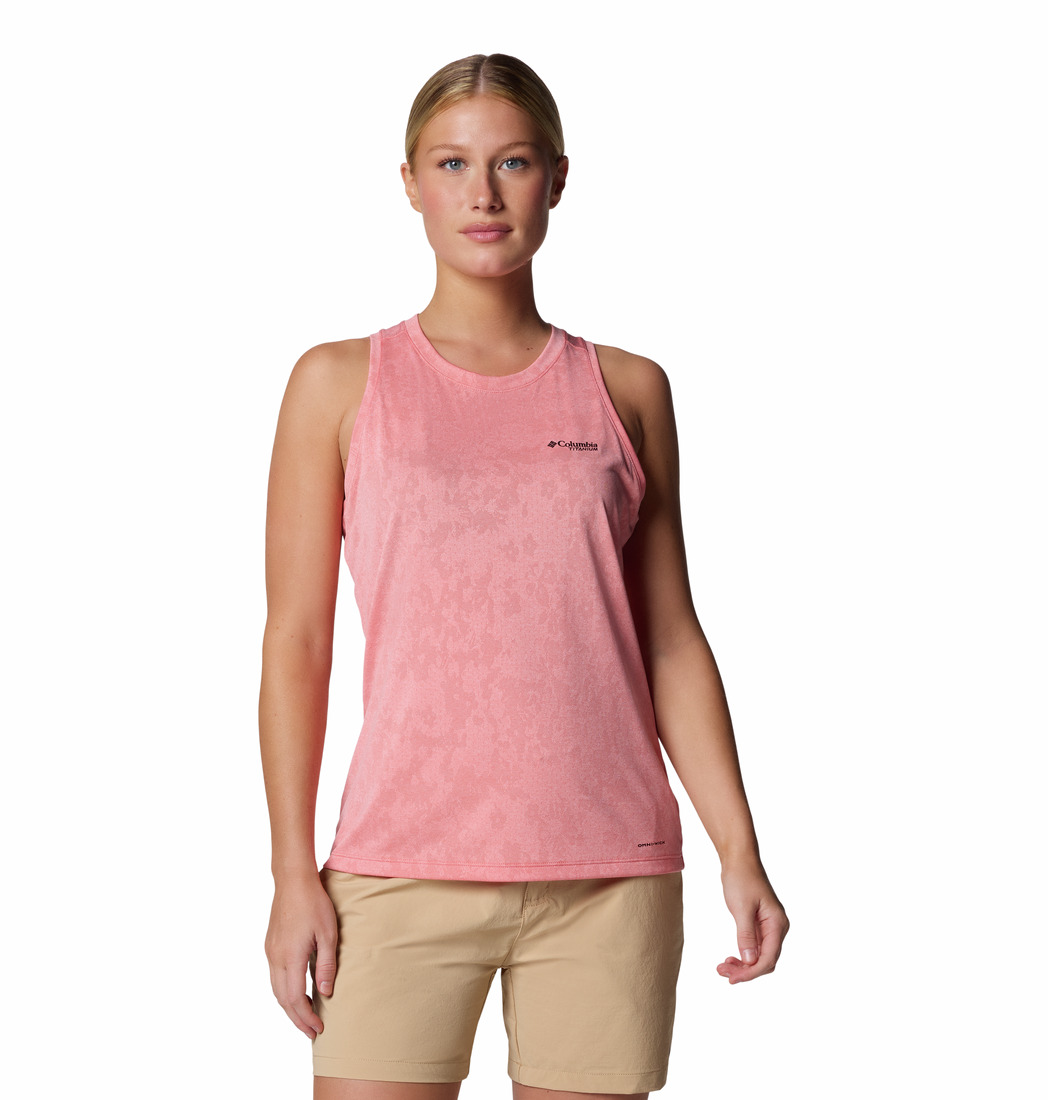 Une femme se tient debout face vers l'avant, vêtue d'un débardeur de sport rose sans manches et d'un short beige sur un fond blanc uni.