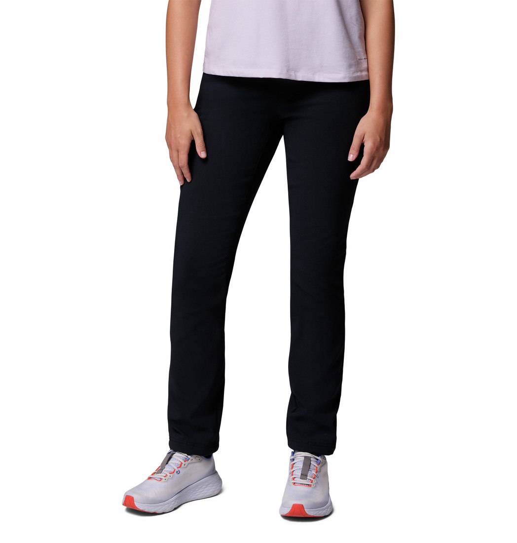 Une personne porte une chemise rose pâle à manches courtes, le PANTALON D'HIVER TAILLE HAUTE COLUMBIA BACK BEAUTY POUR FEMME, et des baskets blanches avec des accents orange sur un fond blanc uni. La tête n'est pas représentée.