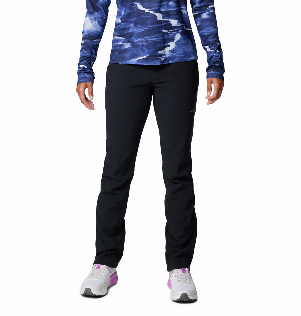 Une personne portant le PANTALON À COQUILLE SOUPLE COLUMBIA VAST CANYON OMNI-HEAT INFINITY POUR FEMME, des chaussures de sport blanches avec des accents roses et un haut à manches longues bleu et blanc se tient sur un fond blanc uni.