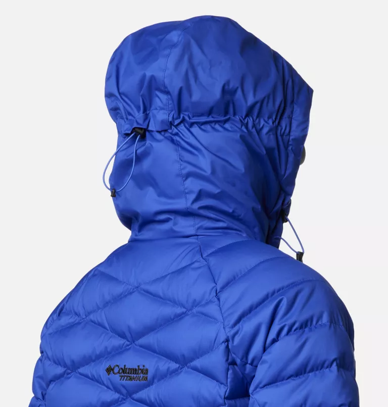 Une personne portant une veste à capuche isolante bleu vif, vue de dos. La veste présente un design matelassé et des cordons de capuche réglables, avec un logo au dos.