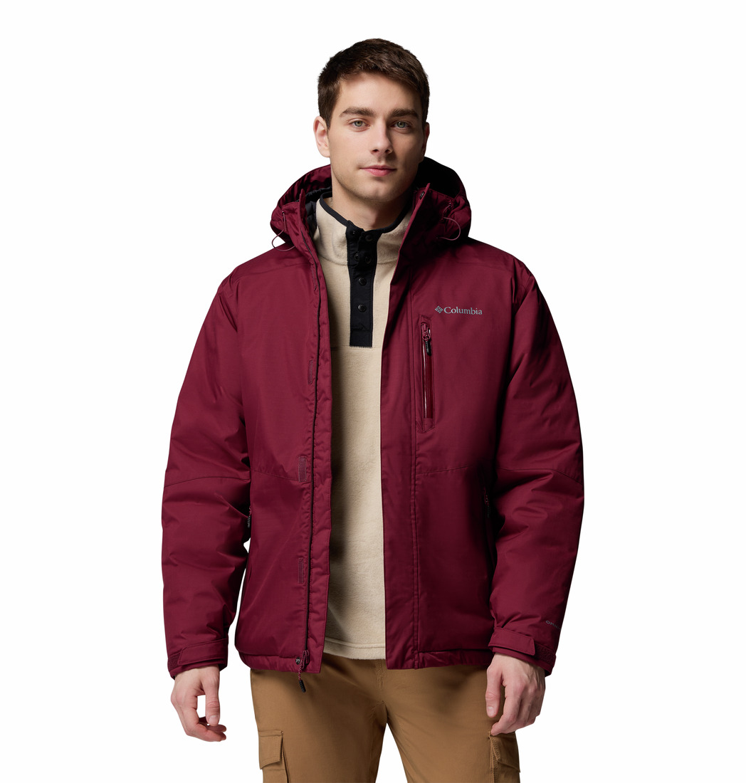 Un jeune homme se tient debout, de face, sur un fond blanc uni. Il porte la veste Columbia OAK HARBOR II INSULATED JACKET de couleur bordeaux avec une capuche, une chemise beige et un pantalon cargo de couleur beige.