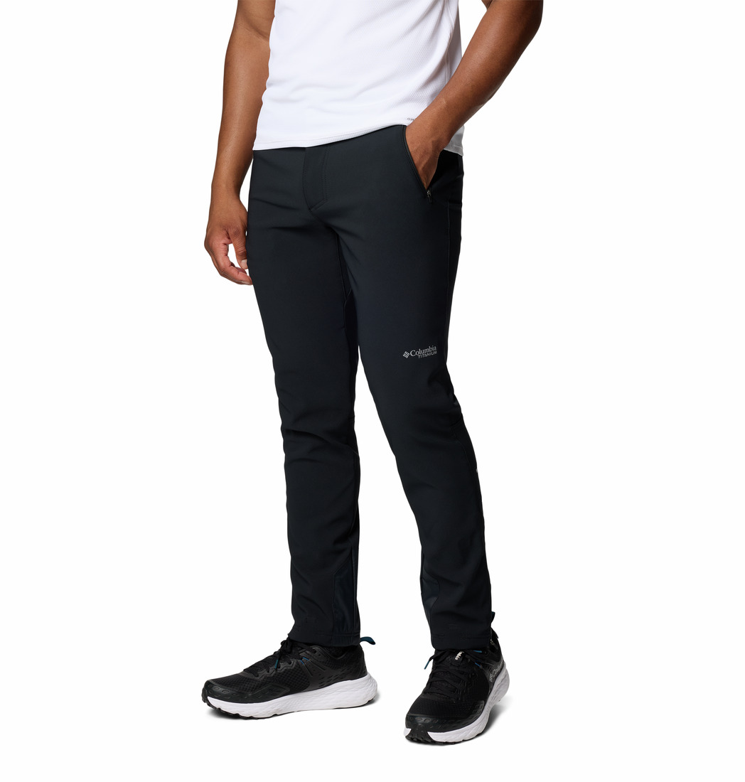 Une personne se tient debout sur un fond blanc uni, vêtue de la veste VAST CANYON OMNI-HEAT INFINITY SOFTSHELL, associée à un pantalon de sport noir et à des baskets noires, les mains dans les poches.