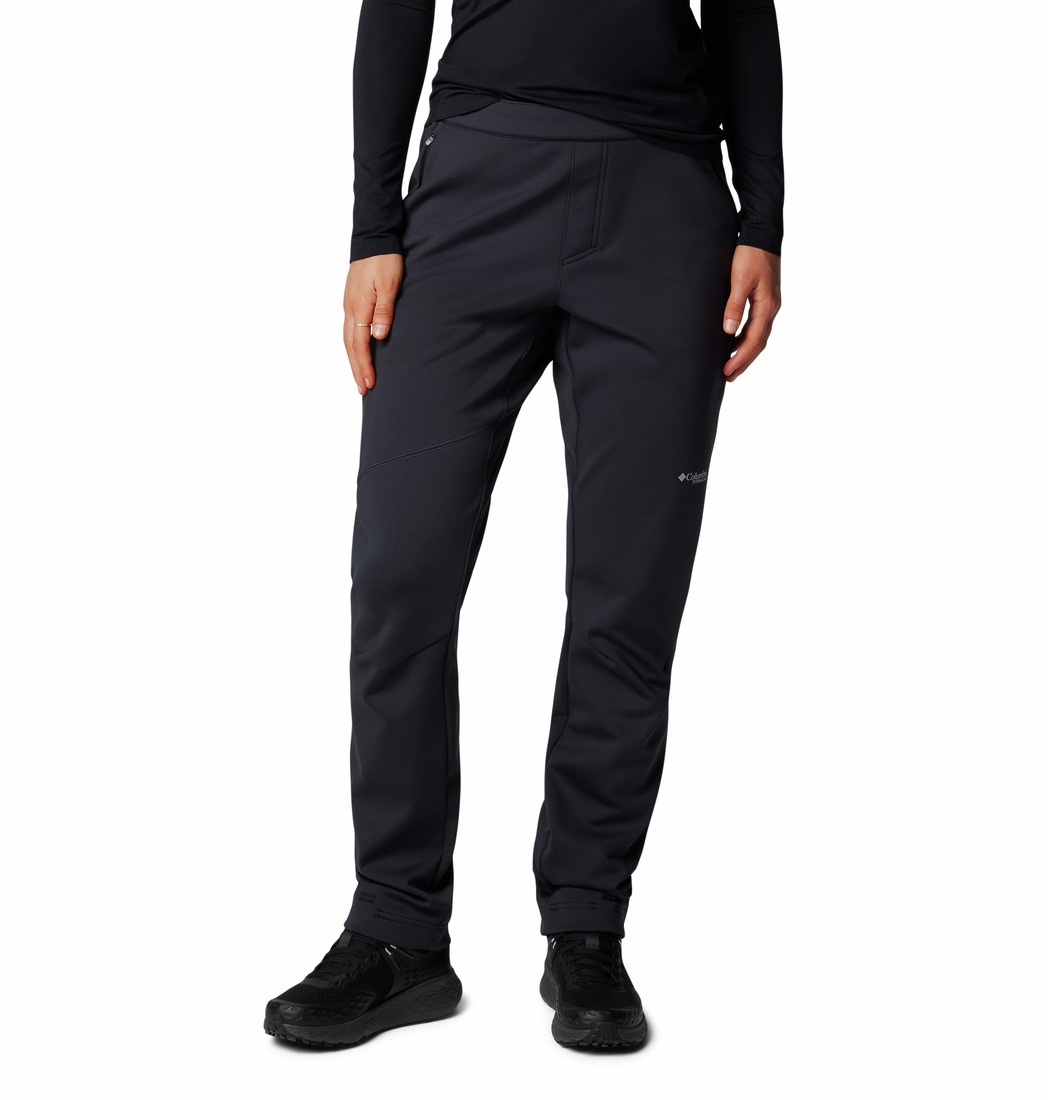 Une personne portant le pantalon VAST CANYON HIGH-RISE SOFTSHELL PANT en noir, associé à une chemise noire à manches longues et à des chaussures noires, se tient debout sur un fond blanc ; seul son corps, à partir des épaules, est représenté.