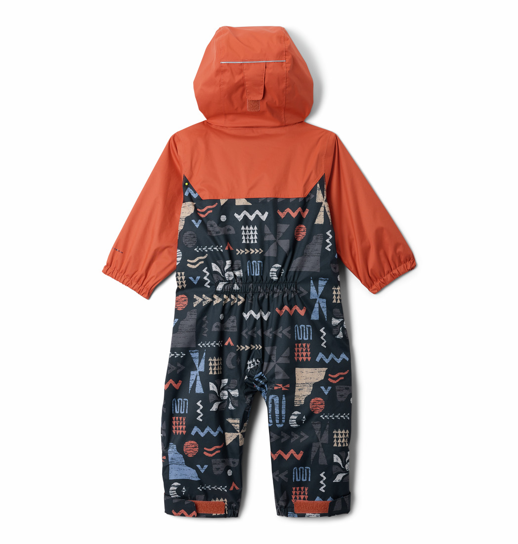 Combinaison de ski pour enfant avec capuche et manches longues. La partie supérieure est orange unie, tandis que la partie inférieure présente des motifs géométriques et en zigzag abstraits et colorés sur un fond bleu foncé. La combinaison de ski est posée à plat, vue de dos.