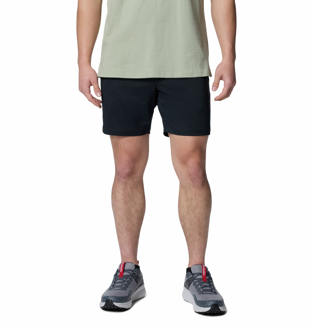Une personne portant un t-shirt vert clair, un short noir et des chaussures de sport grises avec des touches de rouge, se tient debout sur un fond blanc. Seule la silhouette est visible, des épaules aux pieds.