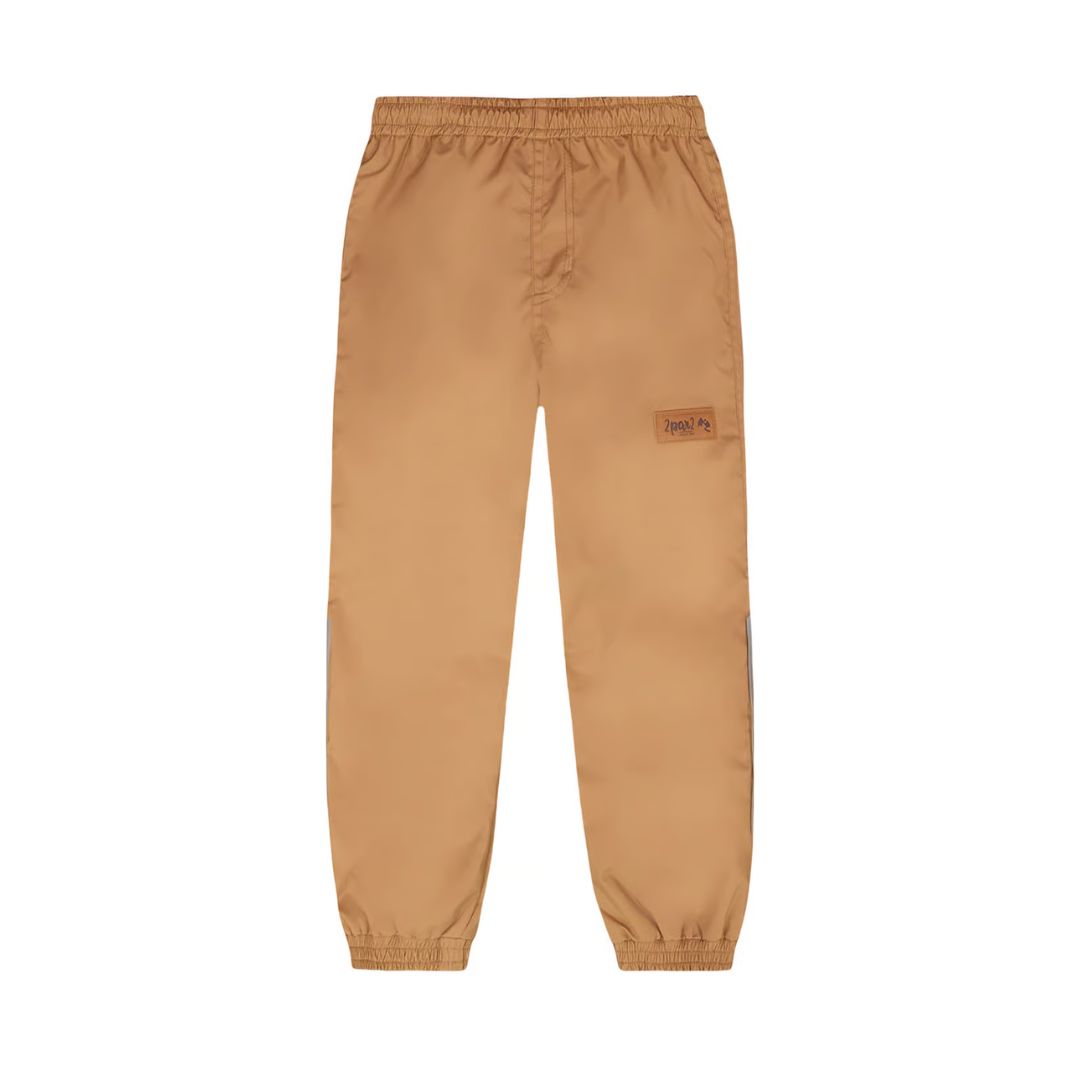 Le pantalon SPLASH PANTS, de couleur marron clair, est doté d'une ceinture et de poignets élastiques, ainsi que d'un petit écusson rectangulaire sur la cuisse, sur fond blanc.
