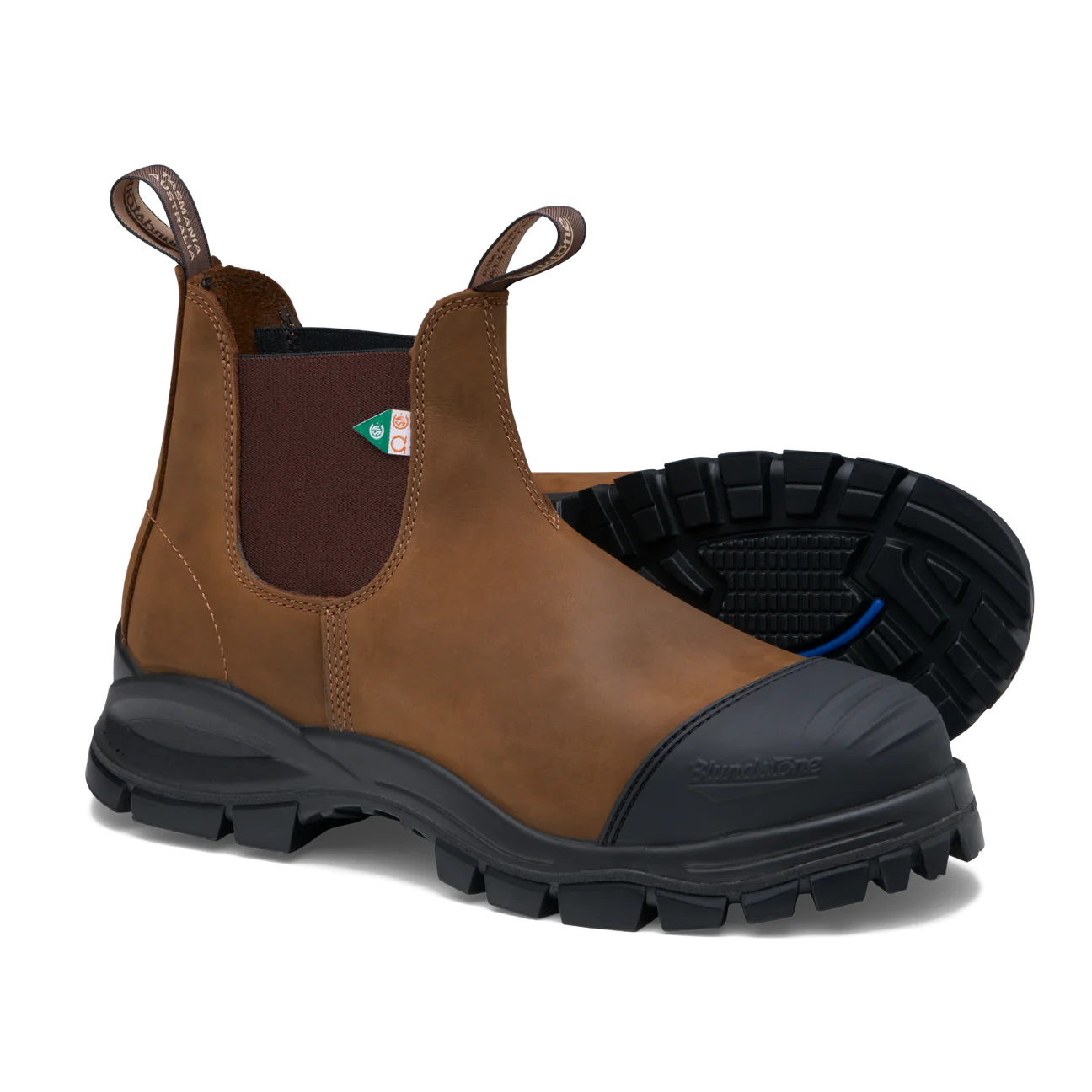Une paire de bottines Chelsea en cuir marron avec des semelles résistantes. Les bottines sont dotées de languettes et d'un logo triangulaire vert. Une des bottines est droite et l'autre est sur le côté, mettant en valeur le motif de la bande de roulement.