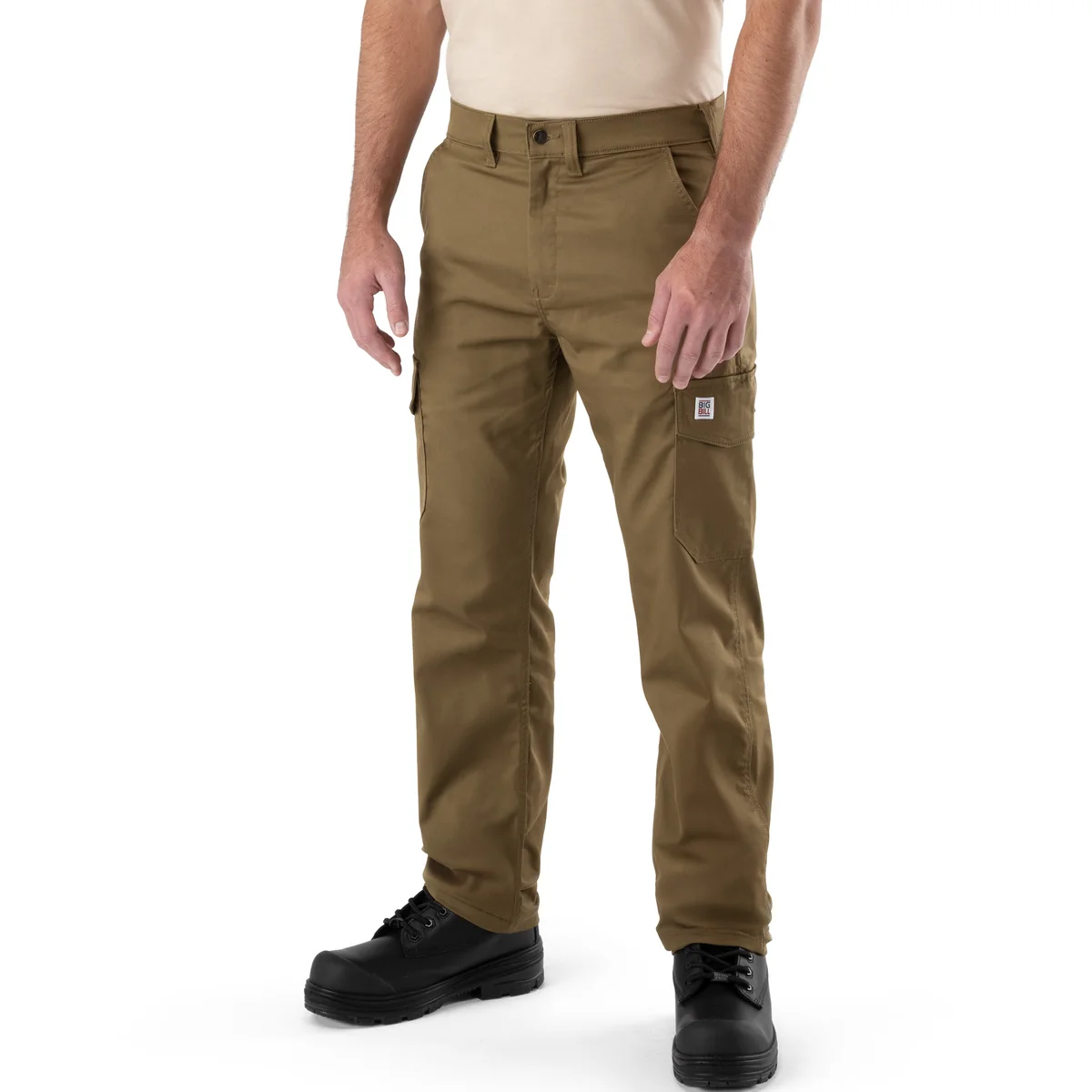 Une personne vêtue d'une chemise beige, d'un pantalon de travail cargo marron « PANTALON CARGO BIG BILL BIG FLEX » et de bottes de travail noires se tient debout, face à l'objectif, devant un fond blanc.
