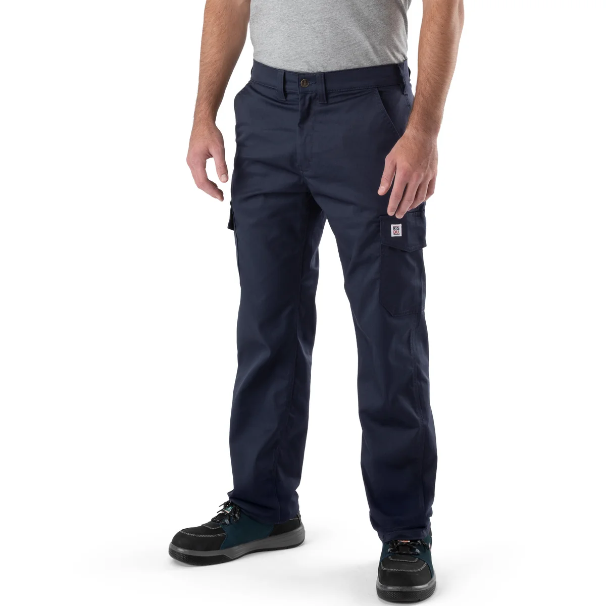 Une personne se tient debout, face à l'objectif, sur un fond blanc. Elle porte un t-shirt gris clair, le modèle « PANTALON CARGO BIG BILL BIG FLEX » bleu marine, ainsi que des chaussures de travail noires et bleu sarcelle.