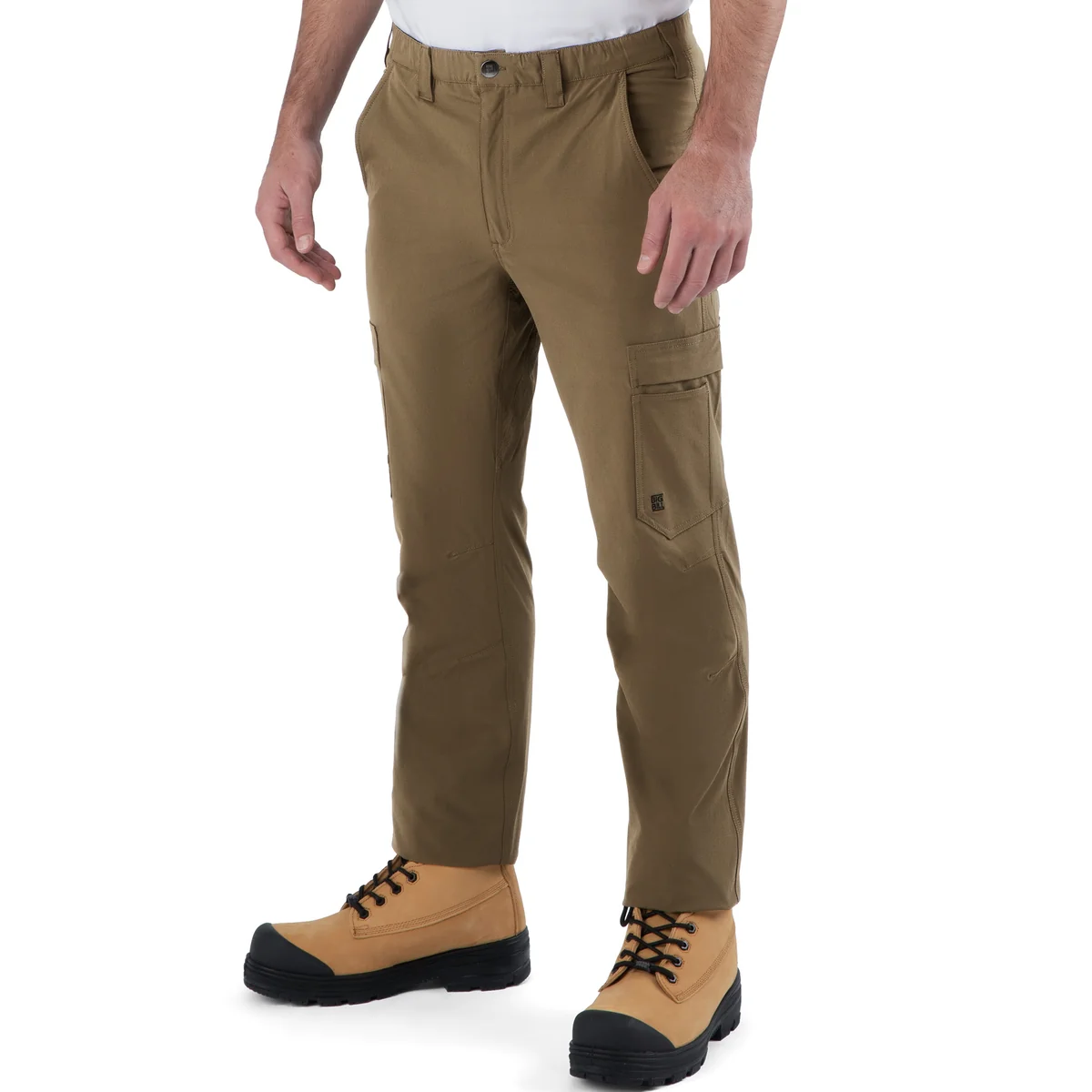 Une personne portant le PANTALON STRETCH ULTRALEGER EXPLORER de couleur kaki, associé à une chemise blanche et des bottes de travail beiges, se tient debout devant un fond blanc uni. Ce pantalon est doté de poches latérales et présente une coupe légèrement fuselée au niveau des chevilles.