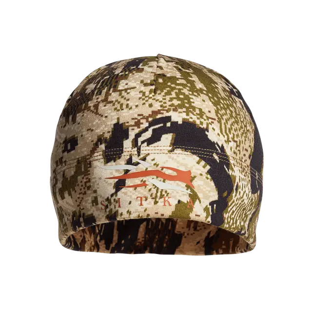 Le MERINO 330 BEANIE est un bonnet de camouflage orné d'un motif camouflage numérique dans des tons de vert, marron et beige, avec un logo SITKA orange et l'inscription « SITKA » sur le devant.