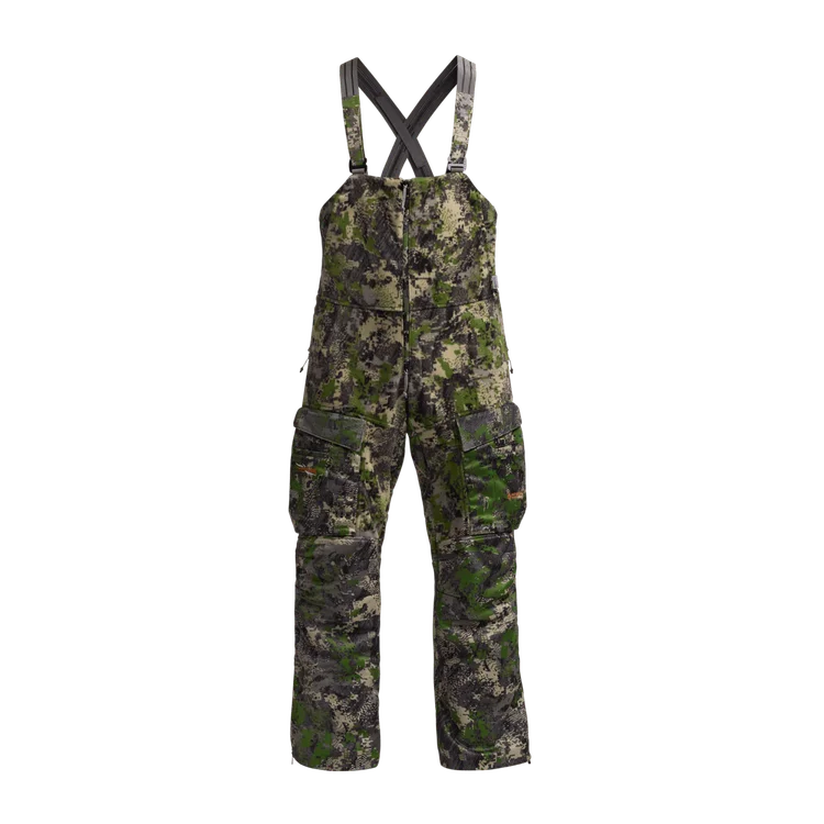 Une paire de salopettes de camouflage avec des bretelles réglables, plusieurs poches zippées et un motif forestier vert, marron et noir, sur fond blanc.