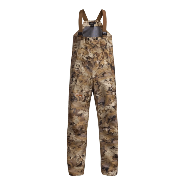 Salopette « SITKA WETLANDS » à motif camouflage, dotée de bretelles réglables marron, conçue pour les activités de plein air ou la chasse, présentée sur un fond blanc uni.