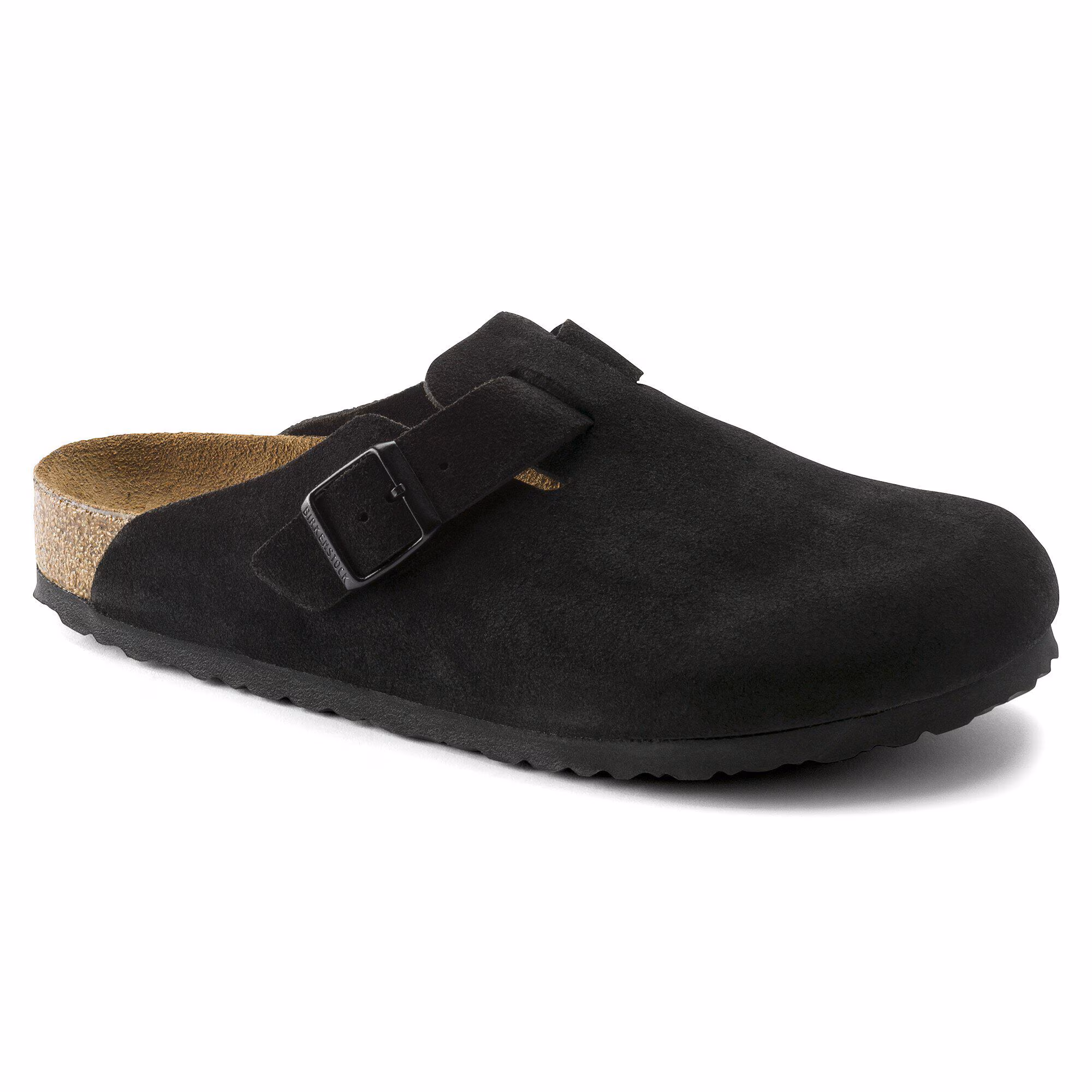 Le modèle BOSTON SOFT FOOTBED SUEDE R est une chaussure sans lacets de style sabot en daim noir, dotée d'une bride à boucle réglable et d'une semelle intérieure en liège, photographiée sous un léger angle de profil sur un fond blanc.