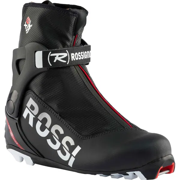 La X-6 SKATE est une chaussure de ski de fond Rossignol noire, dotée d'un lacet zippé, d'accents rouges, d'une bande velcro, d'une semelle blanche et d'une marque "ROSSI" sur le côté.