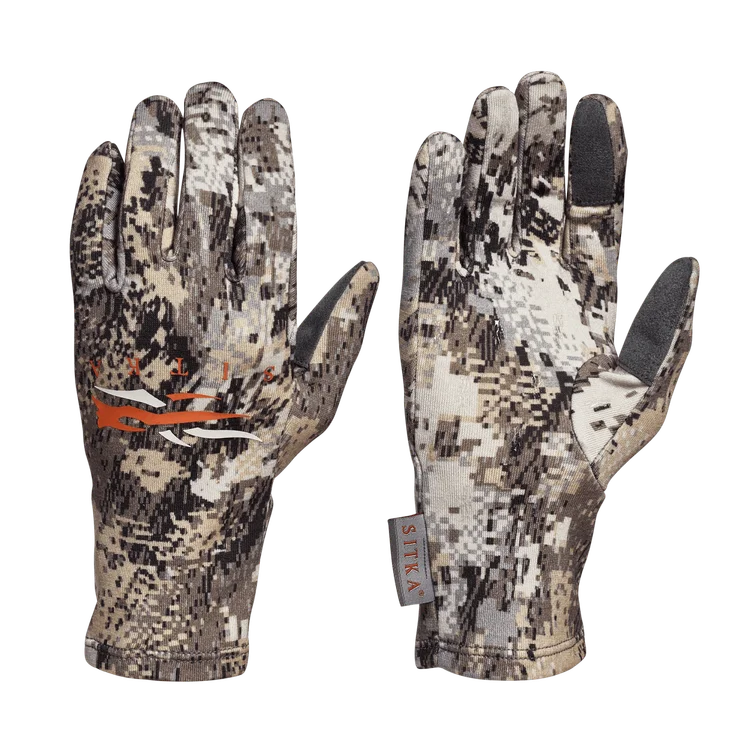 Deux gants à motif camouflage avec impression numérique, comportant un logo orange sur le dos d'une main et un écusson gris sur l'index de l'autre. Les gants sont munis d'étiquettes en tissu portant la mention "SITKA".
