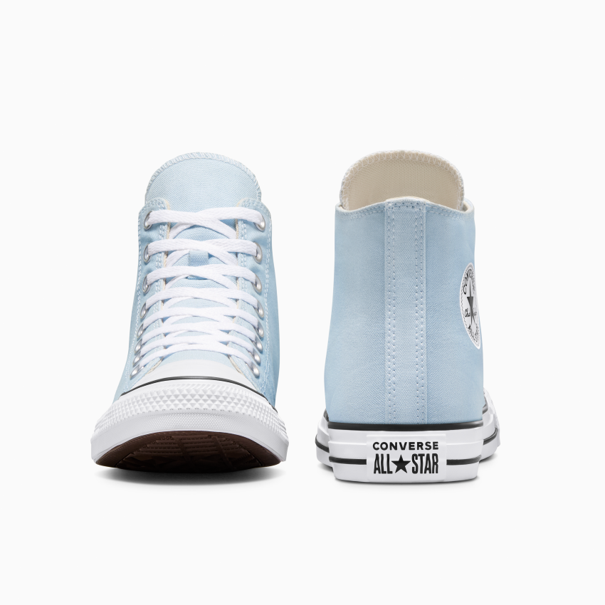 L'image montre une paire de baskets montantes Converse All Star bleu clair. Une des baskets est tournée vers l'avant, laissant apparaître les lacets blancs, tandis que l'autre est tournée pour dévoiler le logo et le talon.