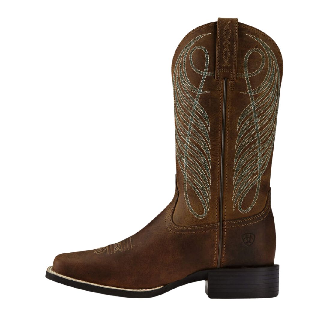 La BOTTE WESTERN ARIAT ROUND-UP AVEC BOUT CARRÉ LARGE POUR FEMME est une botte en cuir marron avec des coutures décoratives bleu clair, un bout carré et un talon noir bas, vue de côté.