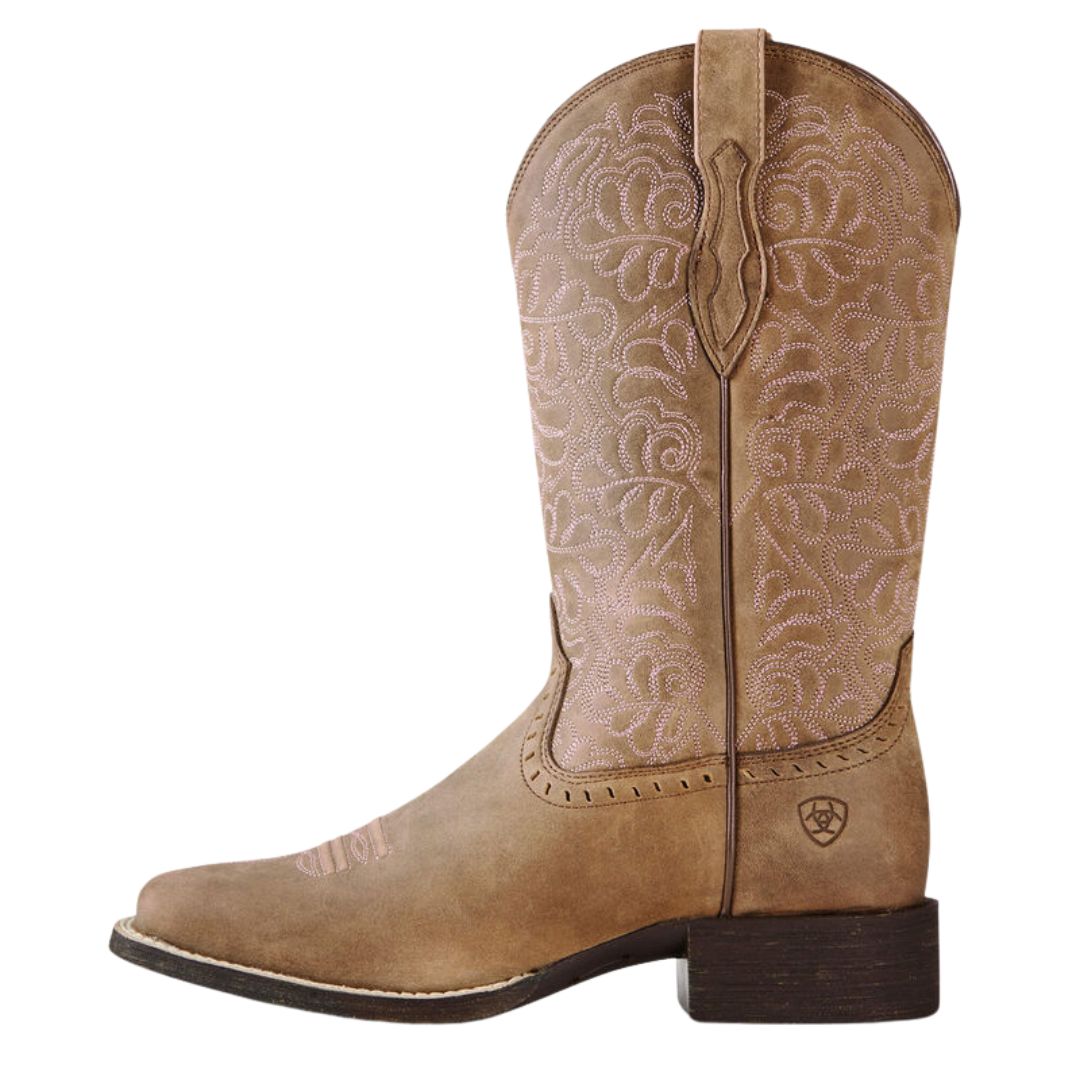 La BOTTE WESTERN ARIAT ROUND-UP AVEC BOUT CARRÉ LARGE POUR FEMME est une botte cowboy brun clair avec bout carré, talon bas, surpiqûres rose pâle, tirant au sommet et petit logo près du talon.