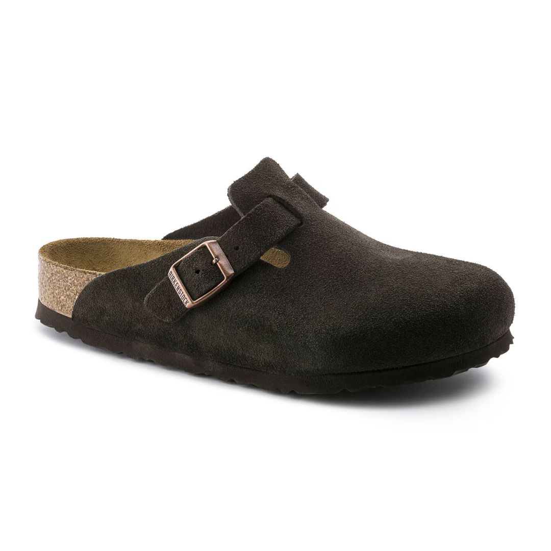 La SANDALE BIRKENSTOCK BOSTON SOFT FOOTBED SUÈDE (ÉTROITE) est une sandale à enfiler en daim marron foncé, dotée d'une semelle intérieure en liège, d'une semelle extérieure noire et d'une bride réglable munie d'une boucle métallique sur le dessus.
