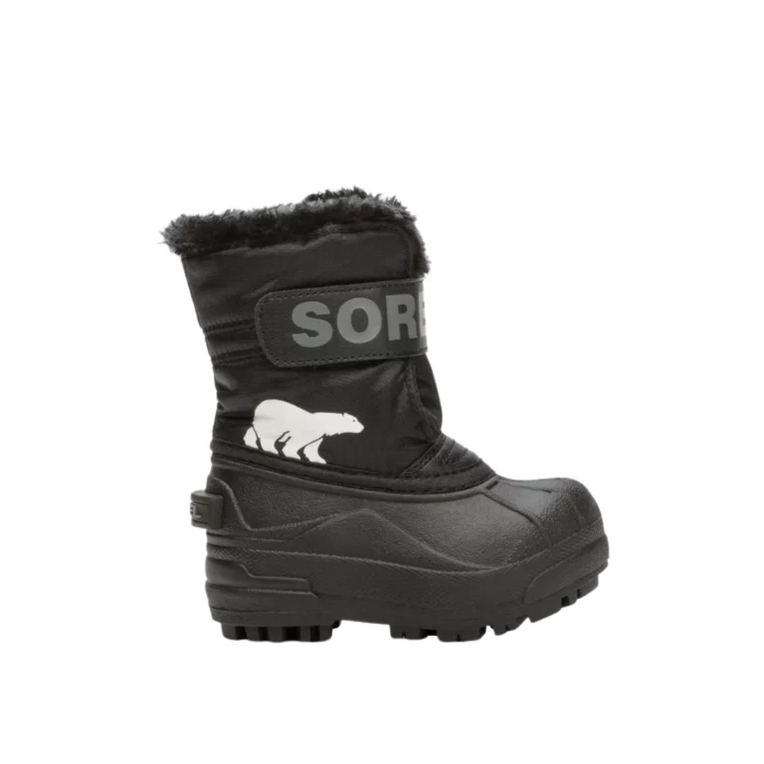 Botte d'hiver noire à semelle épaisse, doublée de fausse fourrure et ornée d'un ours polaire blanc. La botte porte l'inscription "SOREL" en grandes lettres grises sur une bande velcro sur la tige.