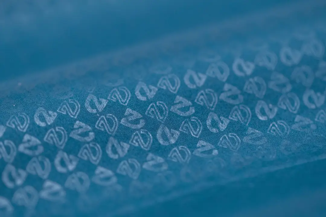 Gros plan d'une surface texturée bleue avec un motif répétitif de petits symboles ou logos blancs et abstraits disposés en rangées diagonales.
