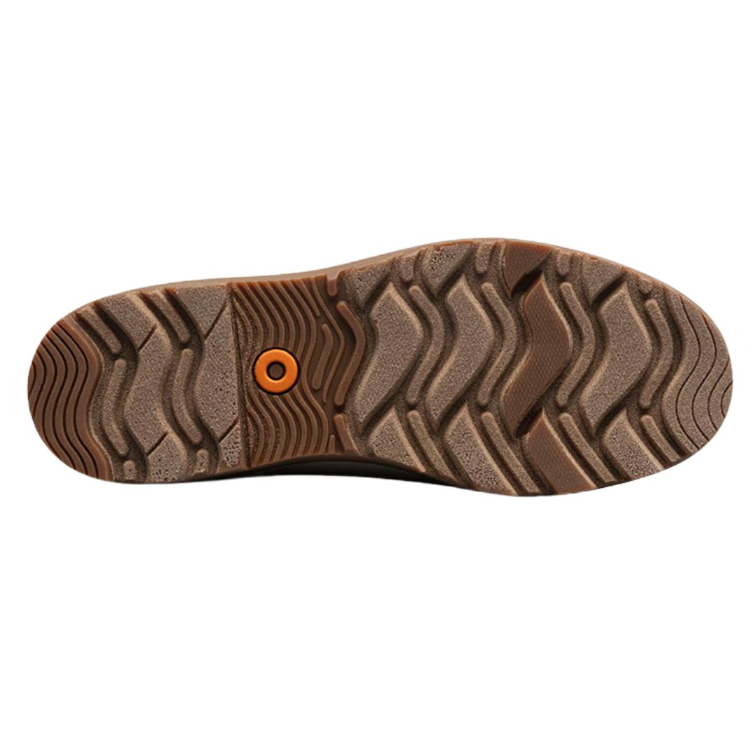 L'image montre la semelle d'une chaussure en caoutchouc marron texturé, avec des rainures ondulées pour une meilleure adhérence. Un petit cercle orange au centre ajoute un détail distinctif au motif général de la semelle.