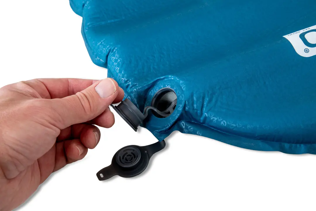 Une main ouvre la valve d’air d’un matelas gonflable bleu, le préparant au gonflage ou au dégonflage.
